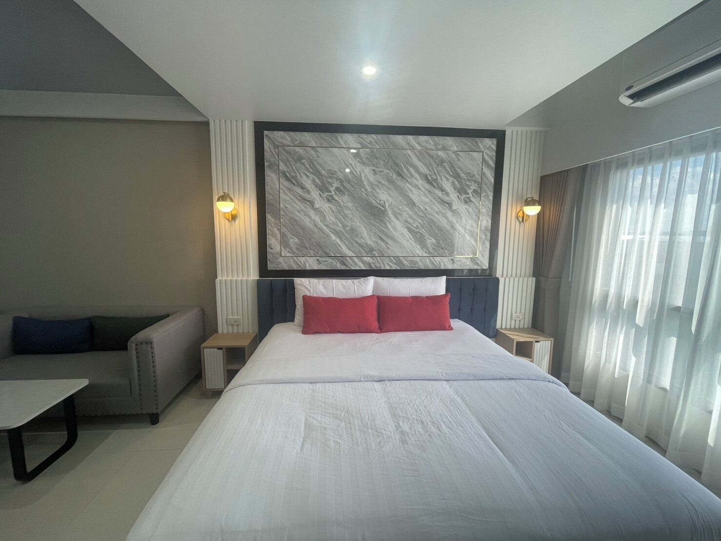 A modern hotel room with a large bed, a sofa, and a marble wall.