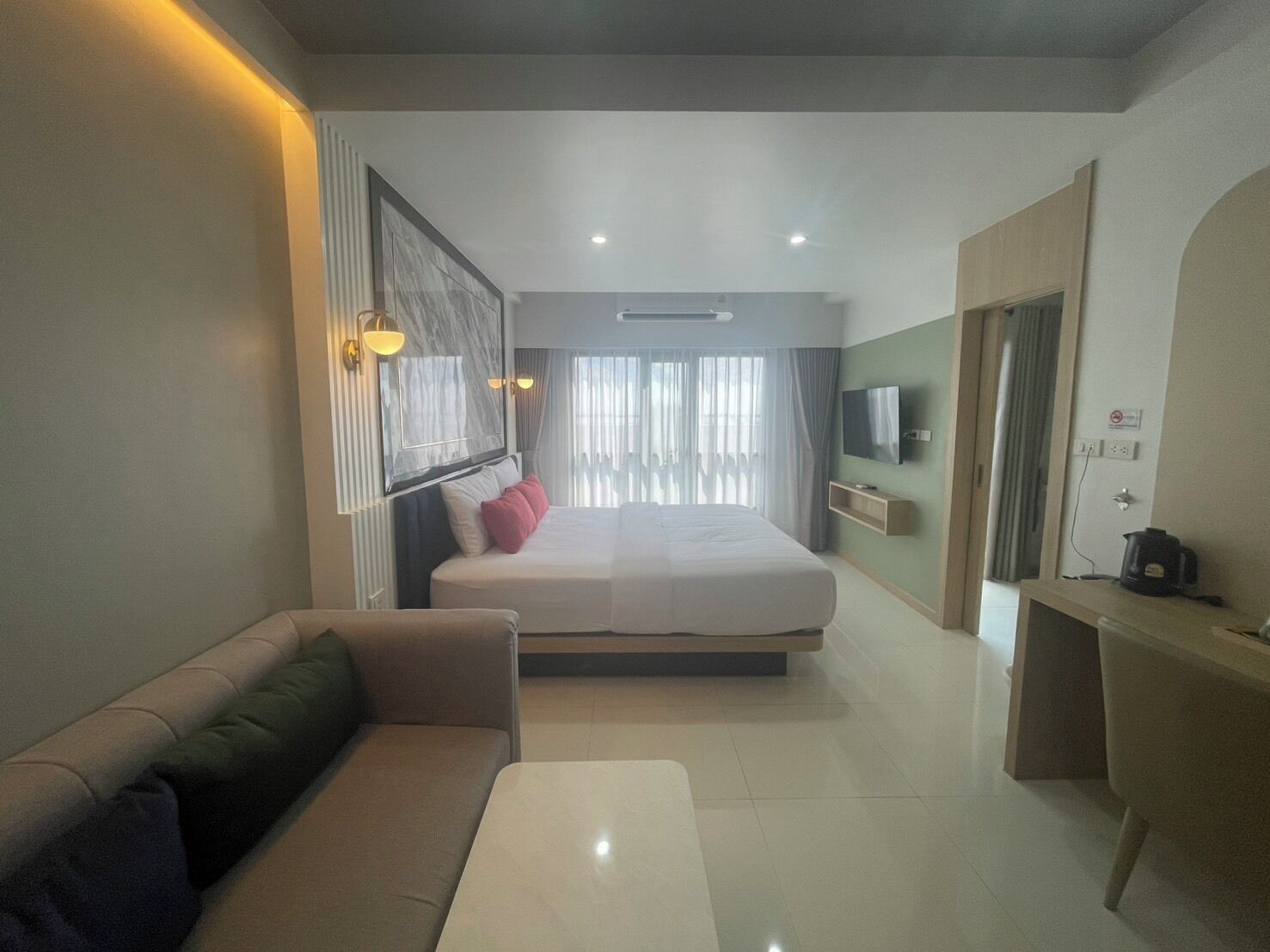 A modern hotel room with a large bed, a sofa, a TV, and a coffee maker.
