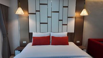 A hotel room with a bed, two red pillows, a wooden headboard, and two pendant lights.