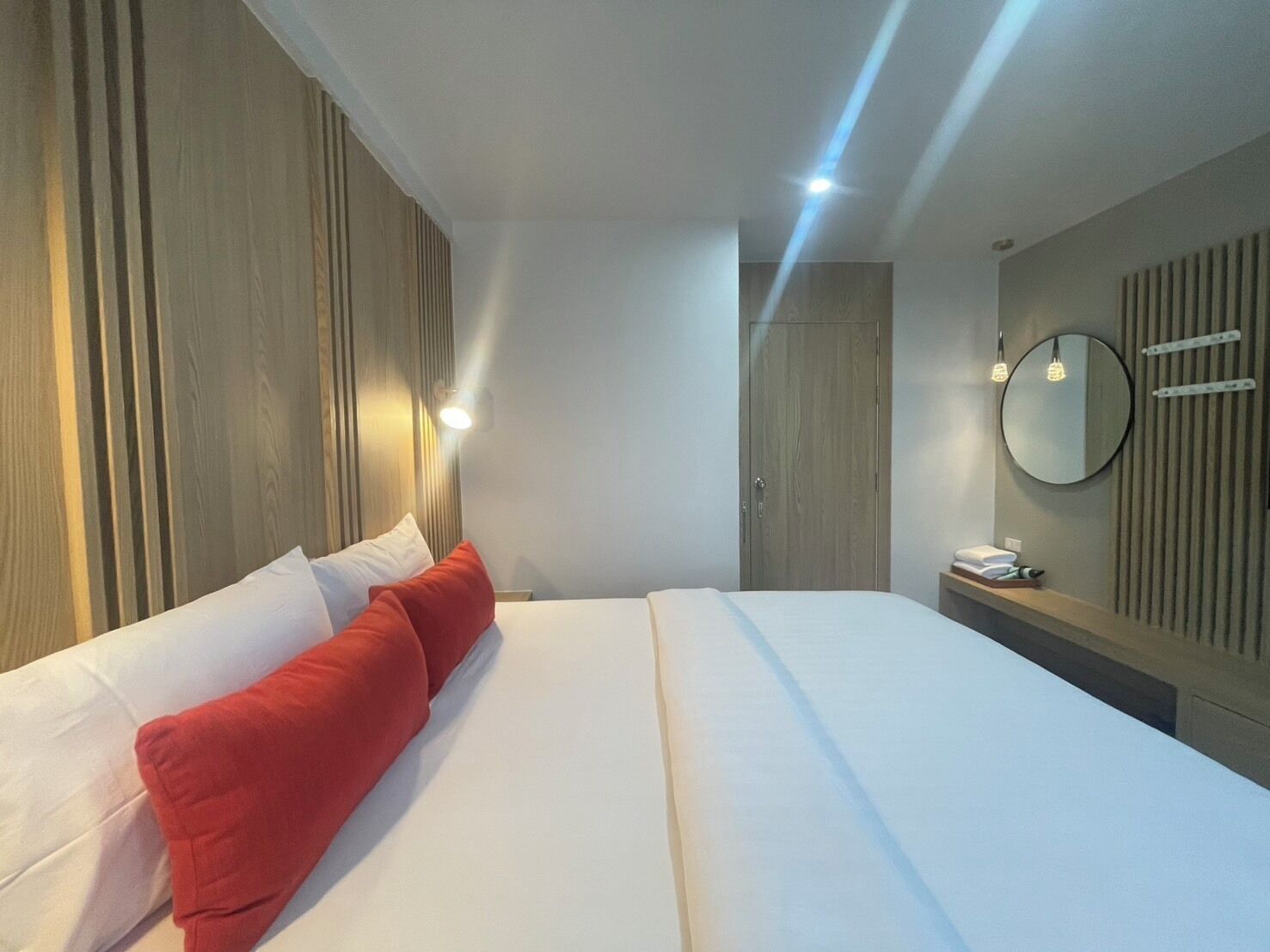 Habitación de hotel con una cama grande, un cabecero de madera, una mesita de noche con teléfono y un espejo redondo en la pared.