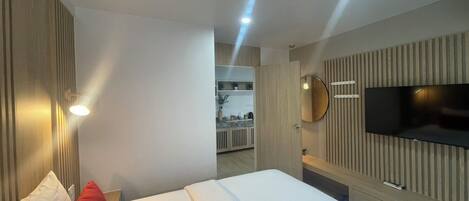A modern hotel room with a large bed, a TV mounted on the wall, and a bathroom visible in the background.