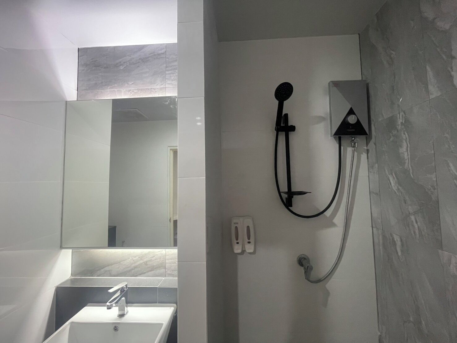 Un baño con un lavabo blanco, un espejo y una ducha empotrada con cabezal de ducha manual.