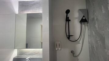 Un baño con un lavabo blanco, un espejo y una ducha empotrada con cabezal de ducha manual.