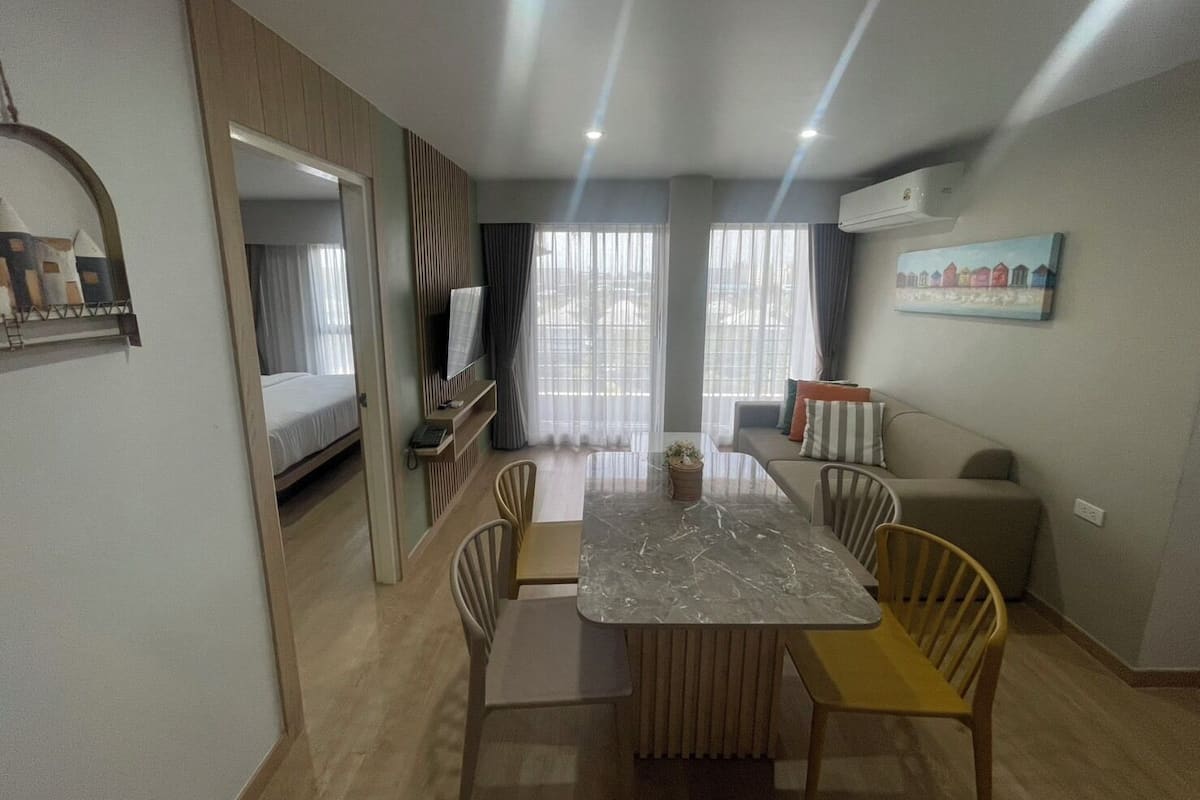 Una habitación de hotel moderna con cama, televisión, mesa de comedor con sillas, sofá y un cuadro en la pared.