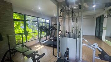 Un gimnasio con equipo de ejercicio, ventanas amplias y vistas a zonas verdes.