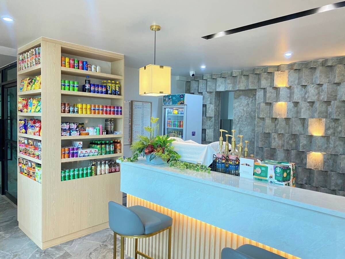 A modern reception area with a wooden shelf stocked with snacks, a blue counter with bar stools, and a stone wall with recessed lighting.