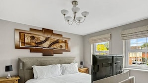 Un dormitorio con cama, televisor, candelabro, mesita de noche y ventana con vistas.