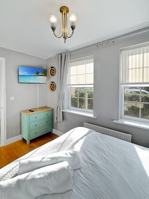 Ein Schlafzimmer mit Bett, Schminktisch, Fernseher und einem Fenster mit Vorhängen.