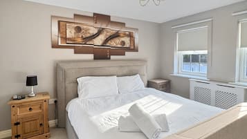 Une chambre à coucher avec un grand lit, une table de chevet, une lampe, un tableau décoratif au mur et une fenêtre.