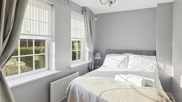 Un dormitorio con cama, dos ventanas con cortinas, un radiador, una lámpara y un candelabro.