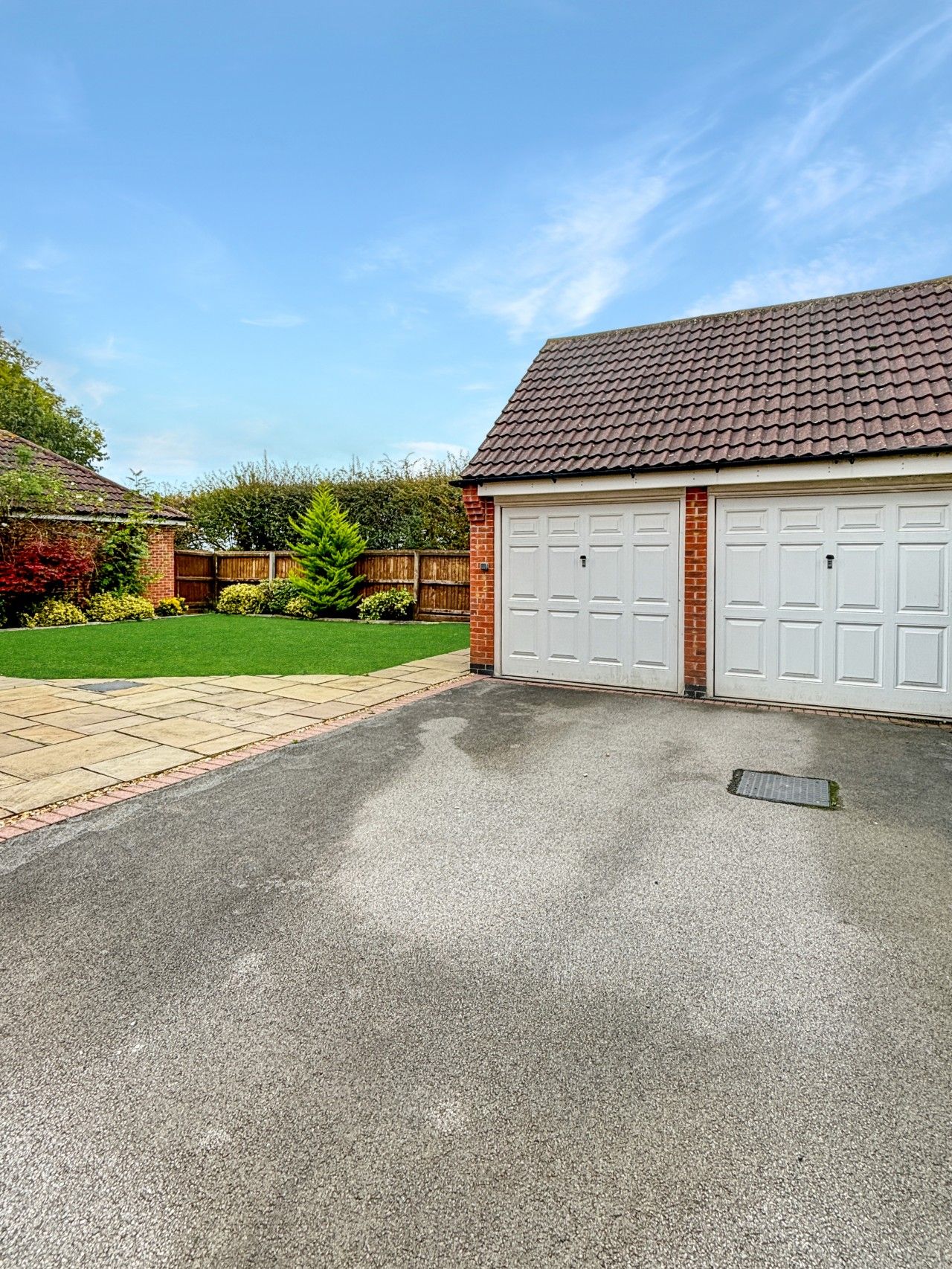 Un garage attenant à une maison, avec une allée pavée et un mur en briques.