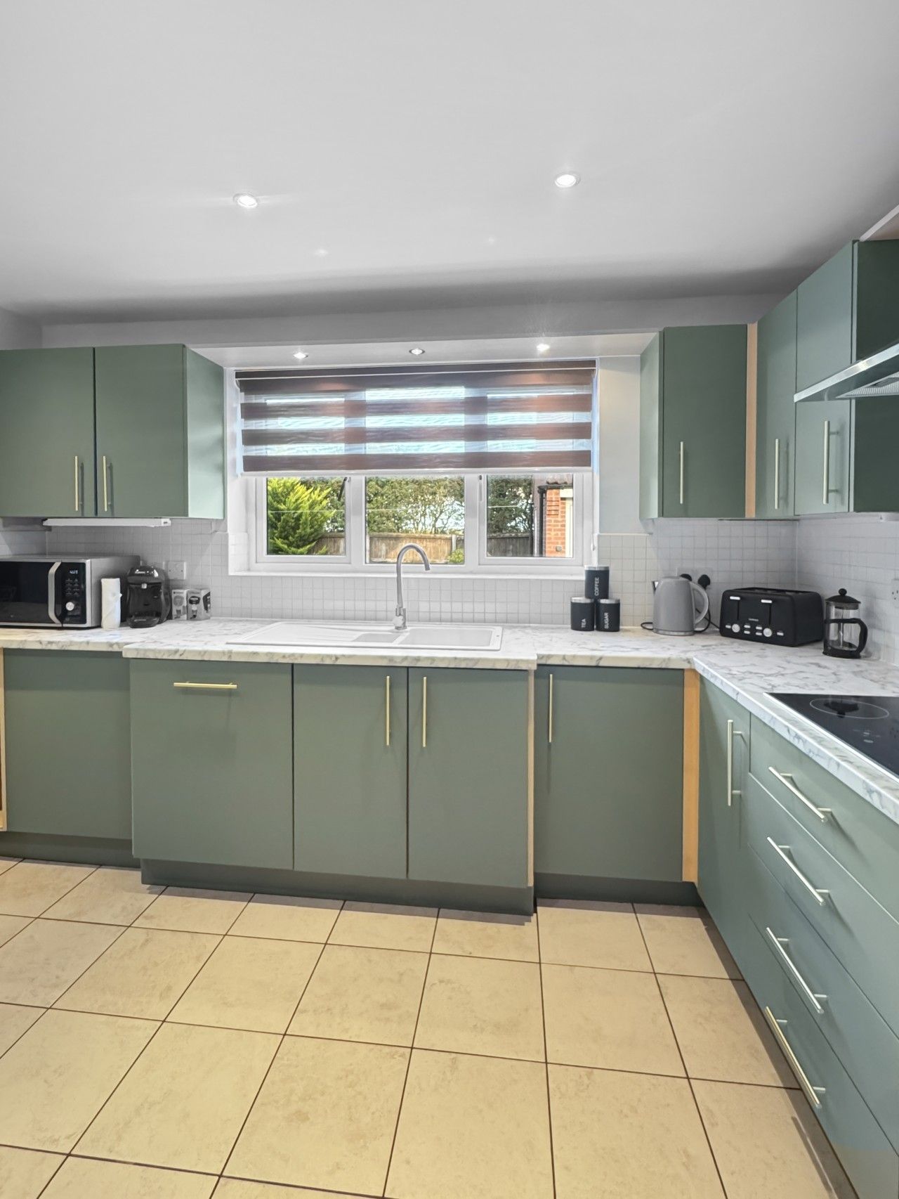 A modern kitchen with green cabinets, a white countertop, and a window with a view of greenery.