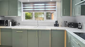 A modern kitchen with green cabinets, a white countertop, and a window with a view of greenery.