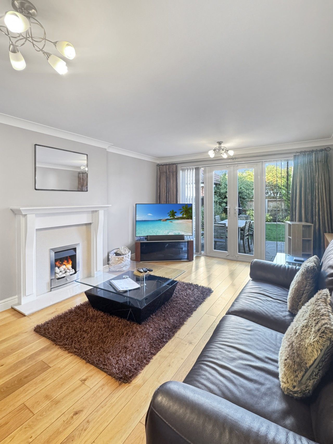 Ein Wohnzimmer mit Kamin, einem Fernseher, der eine Strandansicht zeigt, einer Couch und einem Glastisch.