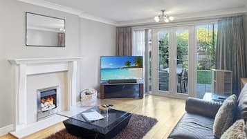 Ein Wohnzimmer mit Kamin, einem Fernseher, der eine Strandansicht zeigt, einer Couch und einem Glastisch.