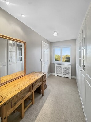 Un couloir avec un banc en bois, un grand miroir et une fenêtre donnant sur un paysage verdoyant.