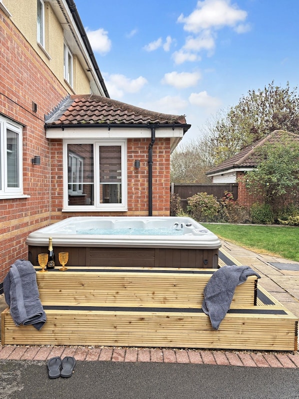 Ein Whirlpool in einem Garten mit einem Ziegelhaus, einer Holzterrasse und einem Rasen.