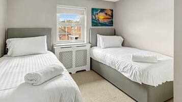 A bedroom with two beds, a window, a radiator, and a painting.