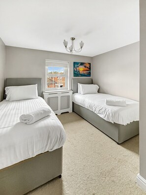 A bedroom with two beds, a window, a radiator, and a painting.
