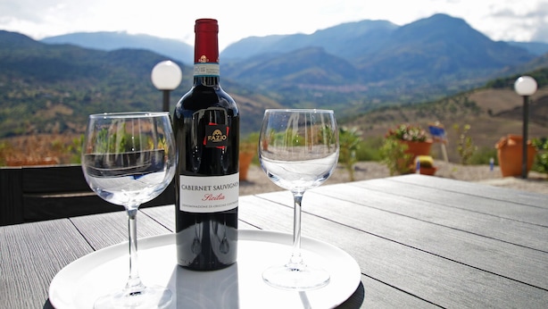 Une bouteille de vin et deux verres sur une table, avec une vue sur les montagnes en arrière-plan.