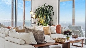 A modern living room with a large plant, a sofa with various cushions, a coffee table, and a view through large windows. - Petrichor Estate - 360 Views, Magnesium Pool & Spa (Sunshine Coast Hinterland)