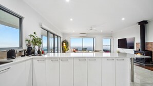 A modern kitchen with a large island, white cabinetry, and a view of the ocean. - Petrichor Estate - 360 Views, Magnesium Pool & Spa (Sunshine Coast Hinterland)