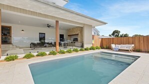 Une maison moderne dotée d’une piscine, d’un patio couvert et d’une clôture en bois.