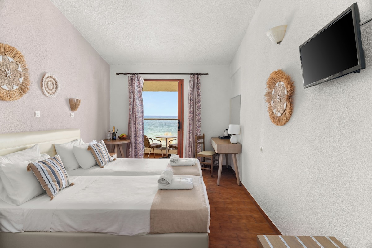 Ein Hotelzimmer mit zwei Betten, einem Fernseher, einem Schreibtisch und Meerblick.