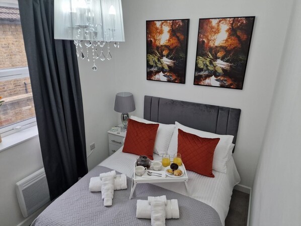 Et hotelværelse med en seng, et natbord med lampe, et bakke med morgenmad og kunst på væggen.