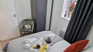 Un letto rifatto con cura, un vassoio con prodotti per la colazione, una sedia grigia e una finestra con tende.