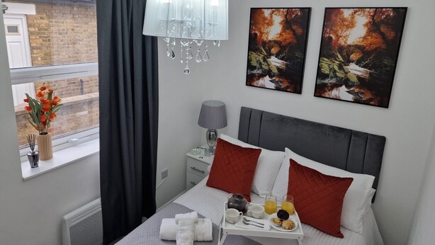 Una camera d'hotel moderna con un letto, un comodino con una lampada, una finestra con tende e un'opera d'arte appesa al muro.