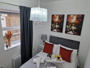 Et moderne hotelværelse med seng, natbord med lampe, et vindue med gardiner og et kunstværk på væggen.