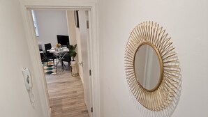 Un corridoio con pavimento in legno, parete bianca e specchio con cornice dorata.
