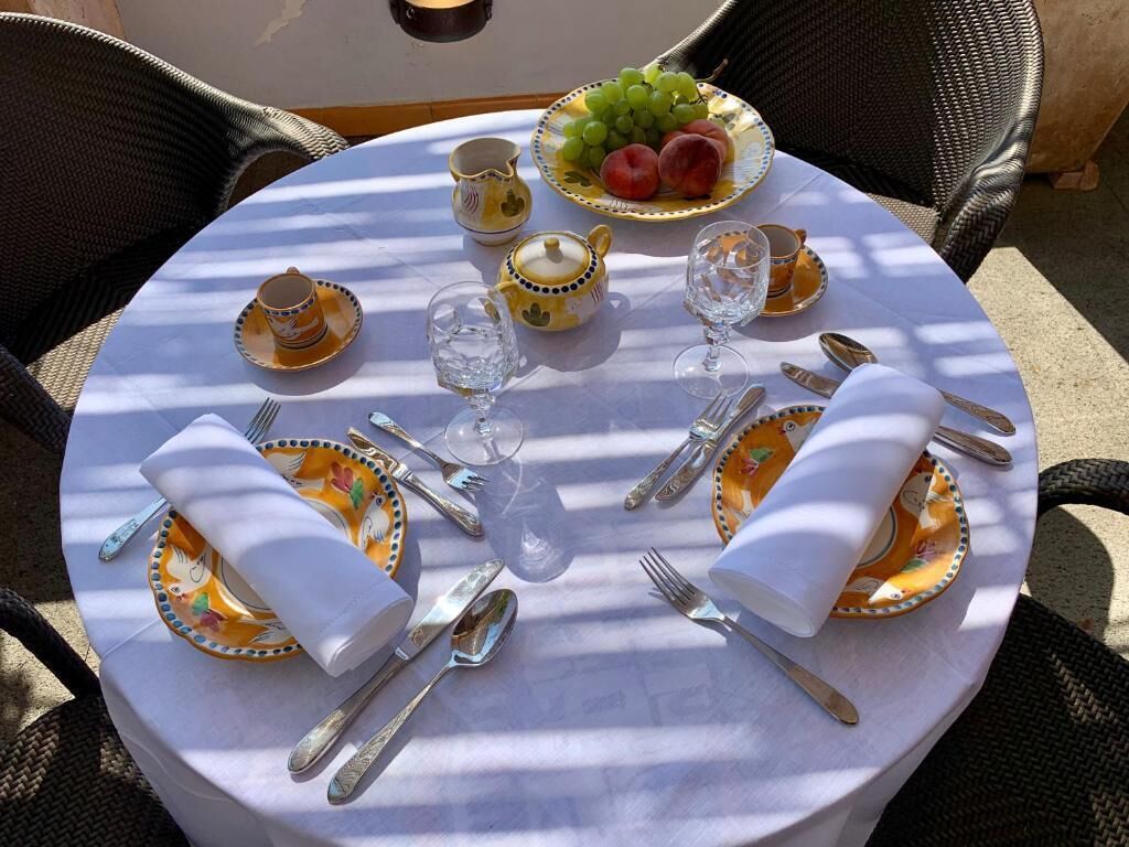 A round dining table set for two with matching plates, cutlery, and a teapot.
