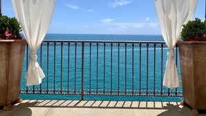 En balkon med havudsigt, hvide gardiner og gelænder i metal.