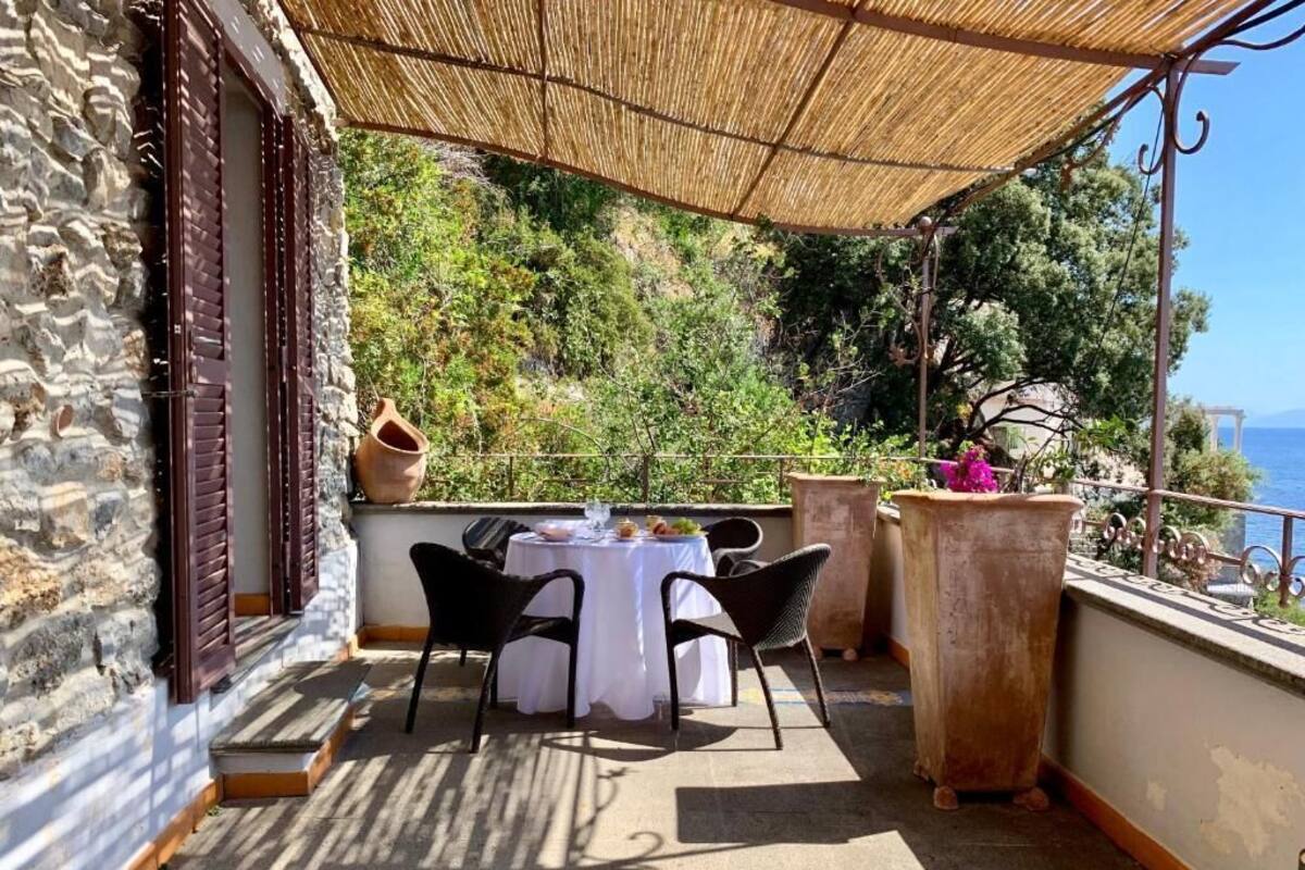A terrace with a table set for two, surrounded by stone walls and a view of the sea.