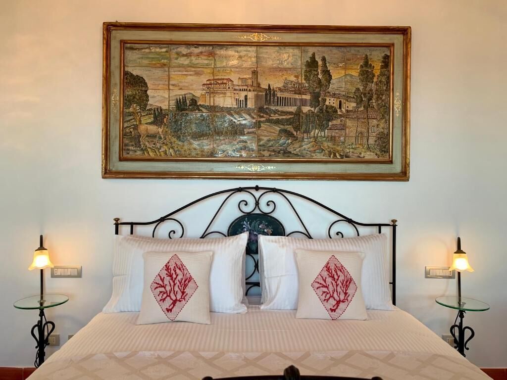 A hotel room with a bed, two bedside lamps, and a framed painting above the bed.