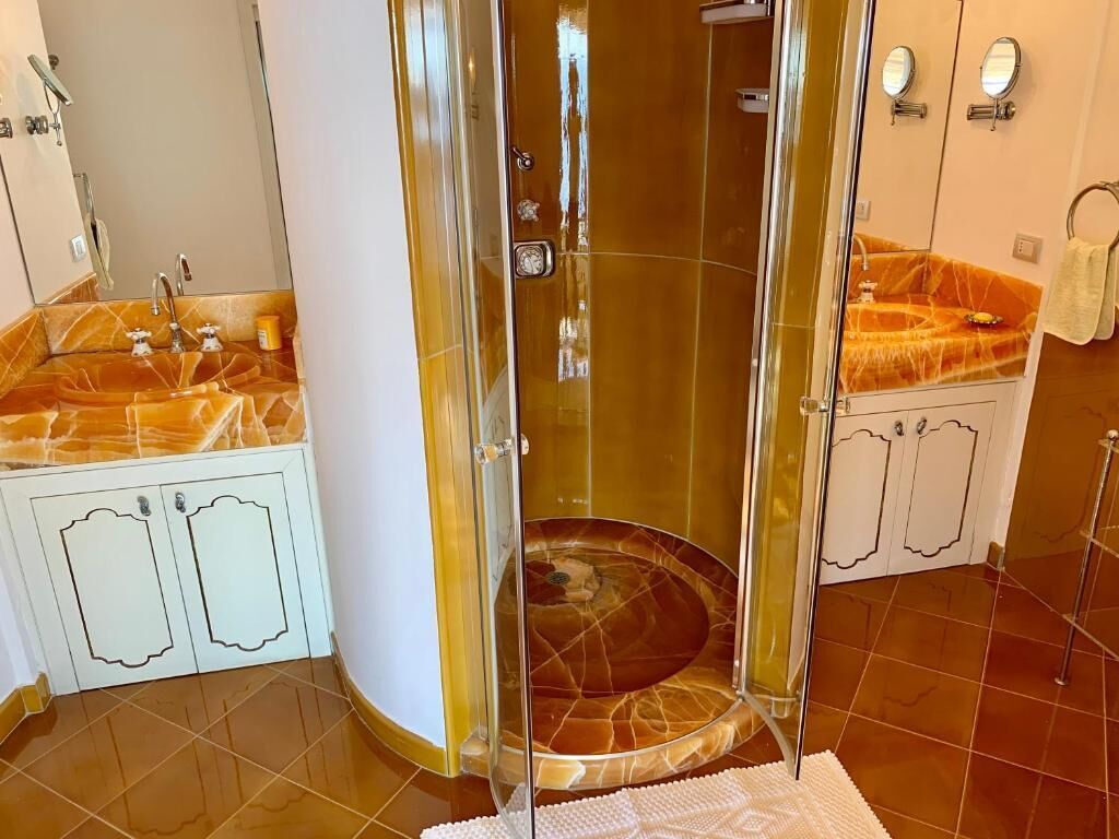 Une salle de bain dotée d’une douche à parois de verre, de vasques en marbre et d’un meuble blanc.