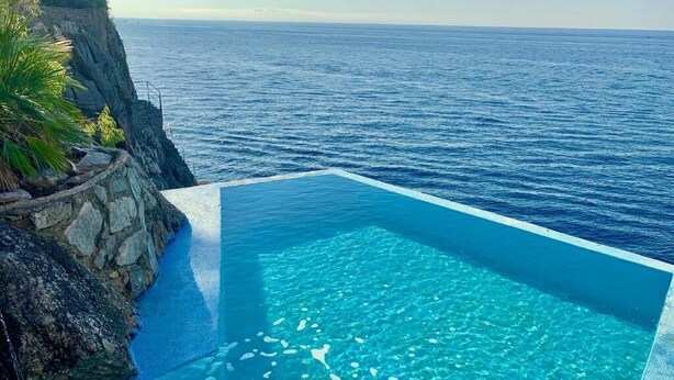 En klar, blå pool uden kant med udsigt over havet og en klippe.