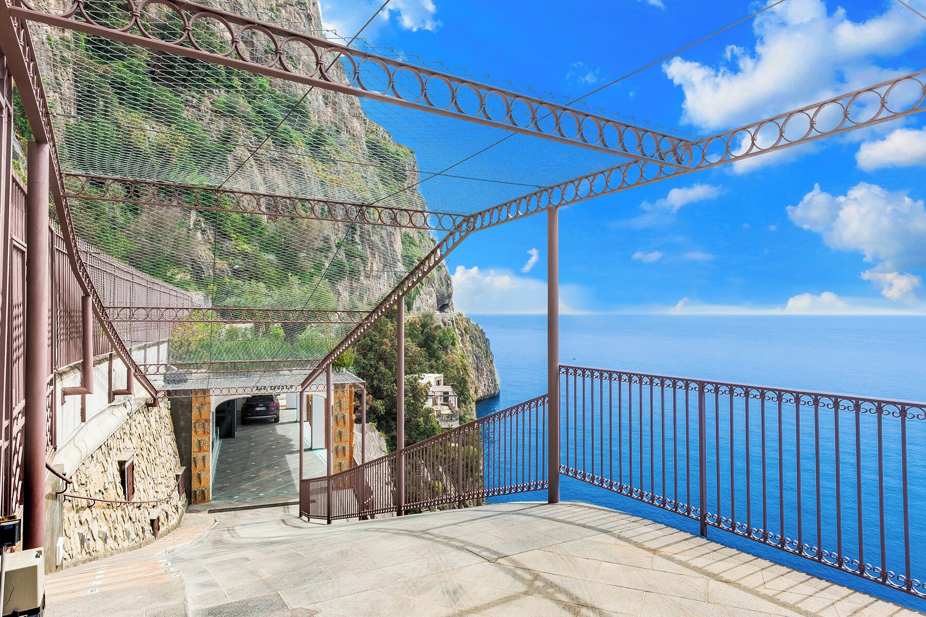 A coastal entrance with a metal gate, stone steps, and a view of the sea.
