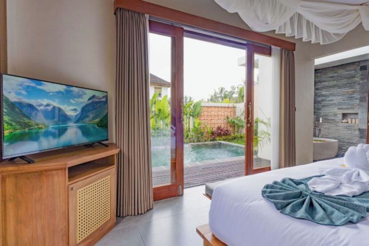 A hotel room with a bed, a TV, a sliding glass door to a pool, and a stone wall.