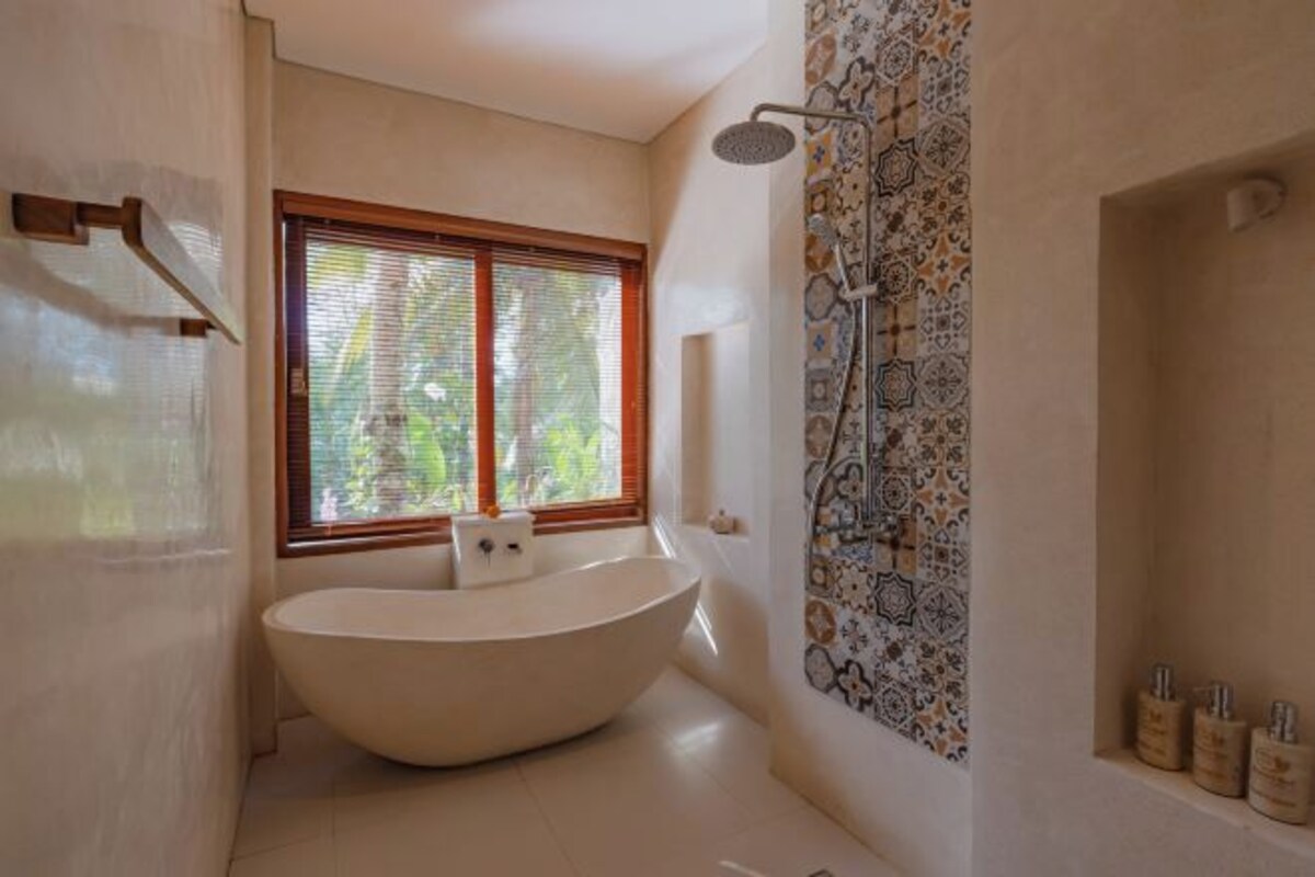 A modern bathroom with a freestanding bathtub, a shower with a patterned wall, and a window with blinds.