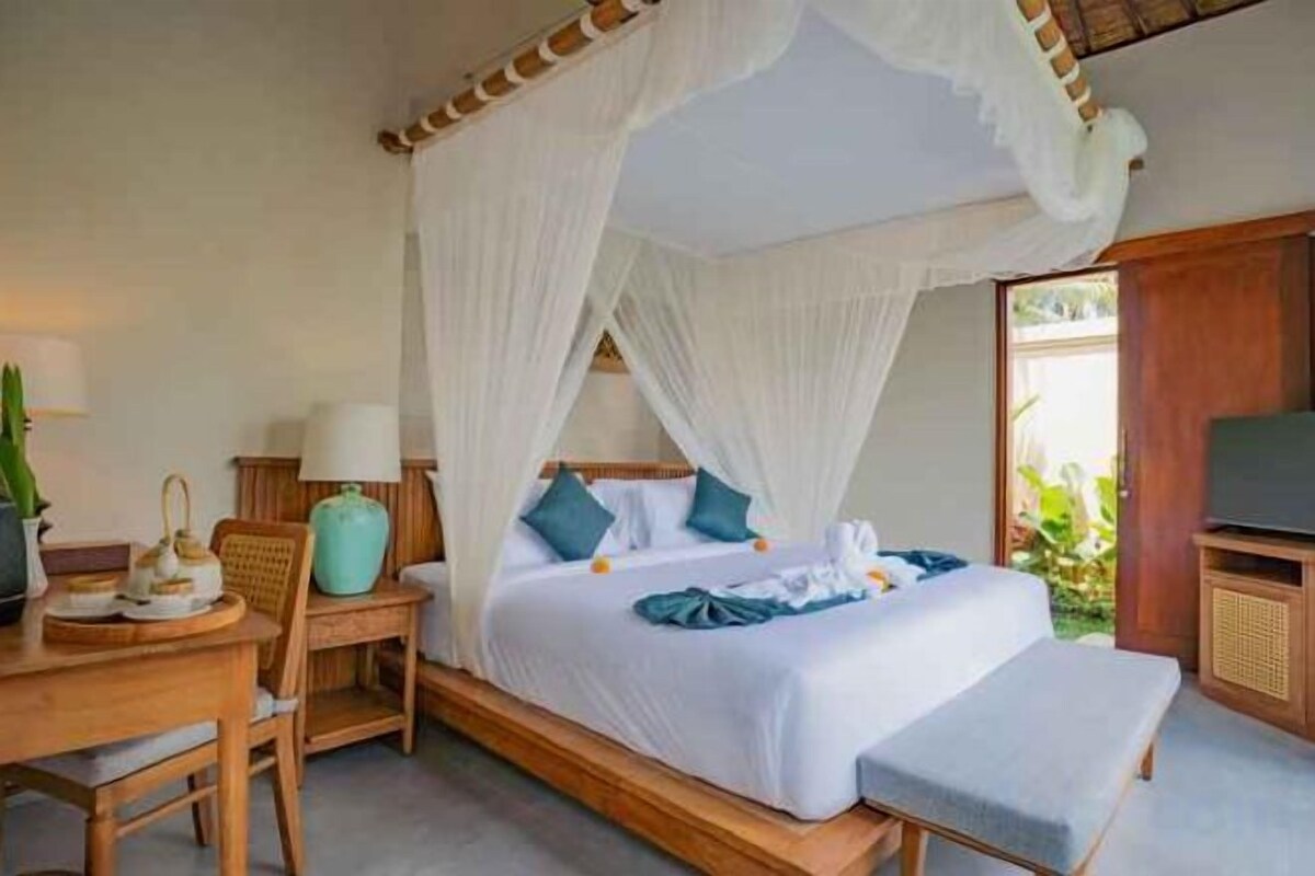 A room with a four-poster bed, a bedside table with a lamp, and a television.