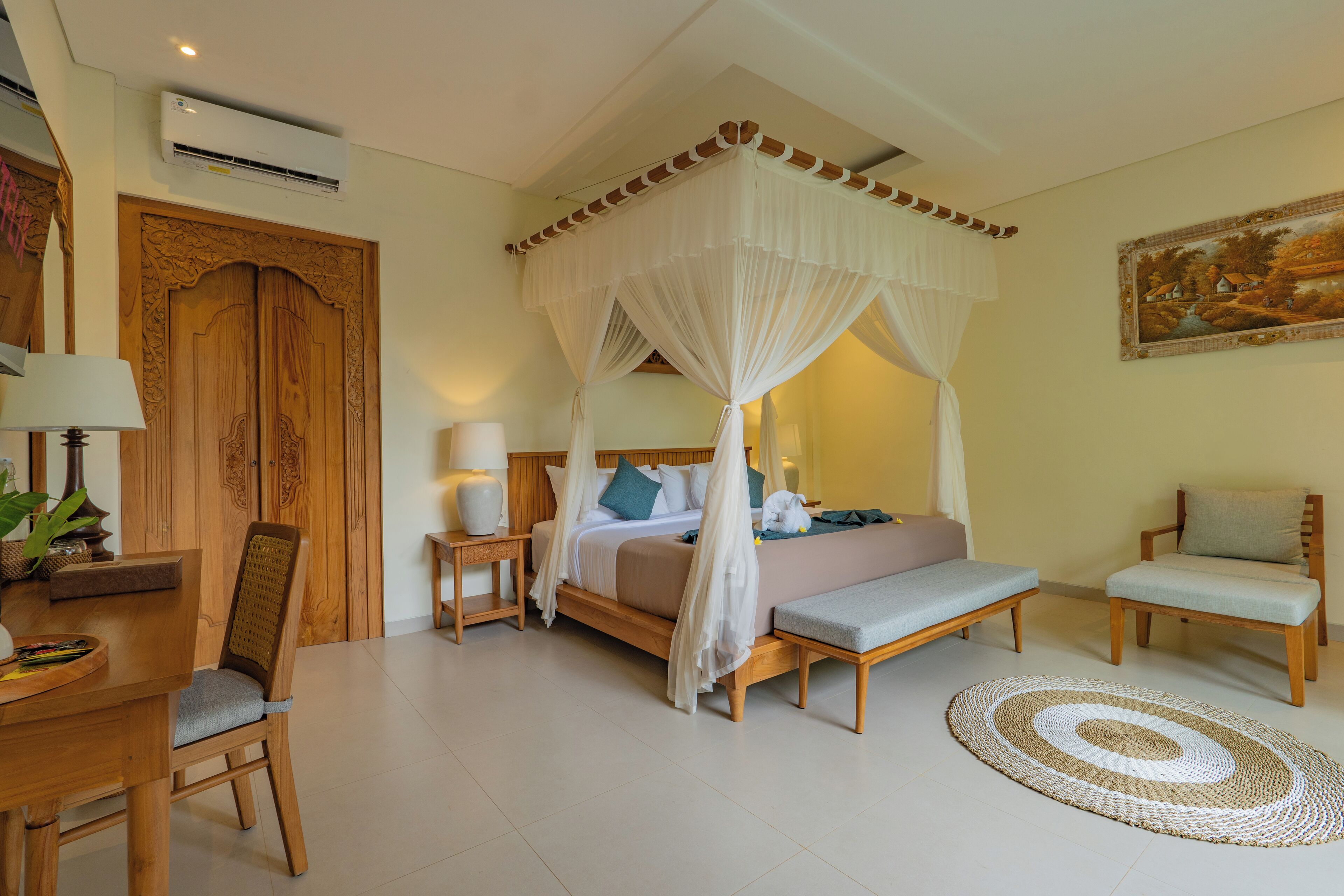 A bedroom with a four-poster bed, a bedside table with a lamp, a chair, a bench, and a decorative rug.