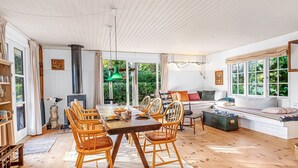 Un comedor amplio con una mesa y sillas de madera, un ventanal con vistas a zonas verdes y un rincón de descanso con sofá y cojines.