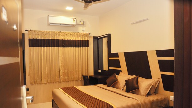 A hotel room with a bed, bedside table, and an air conditioning unit. - Harikrishna Park  (Coimbatore)