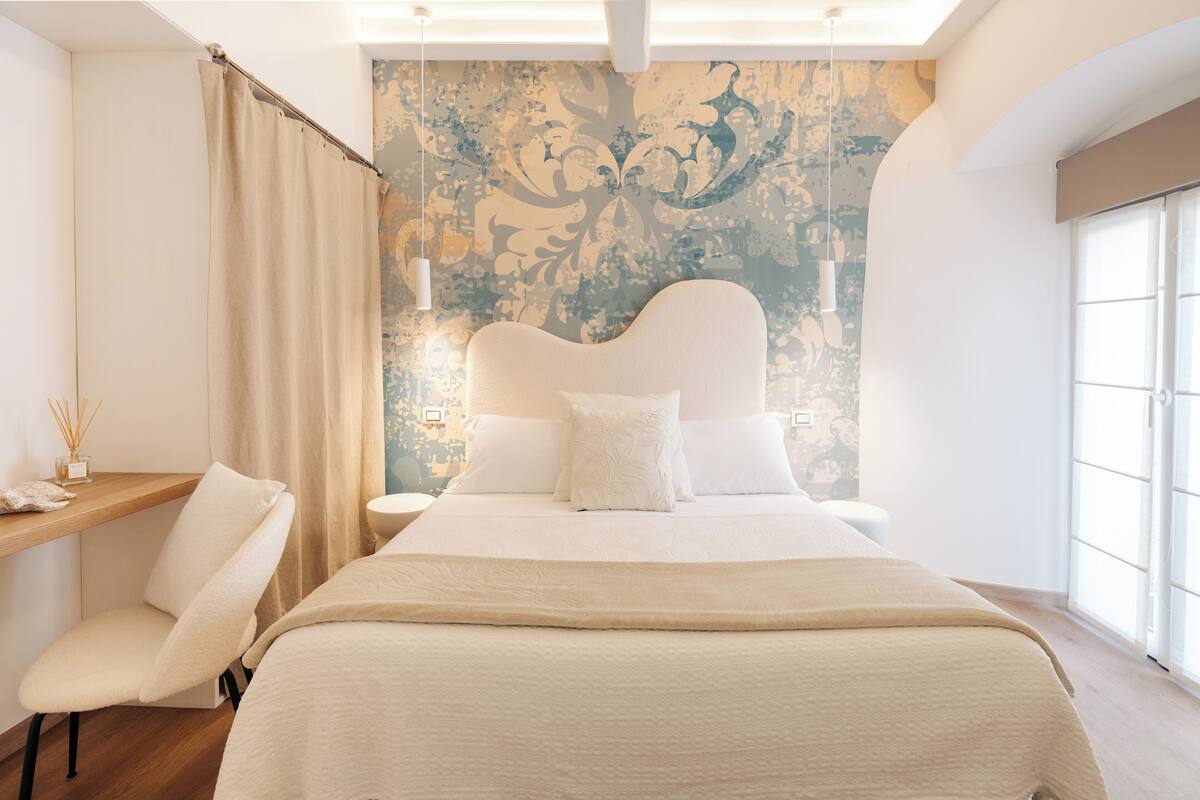 Een moderne slaapkamer met een groot bed, een stoel, een bureau en decoratieve wand.