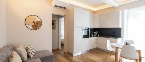 Una cocina moderna con armarios blancos, encimera negra y un comedor con sillas blancas.