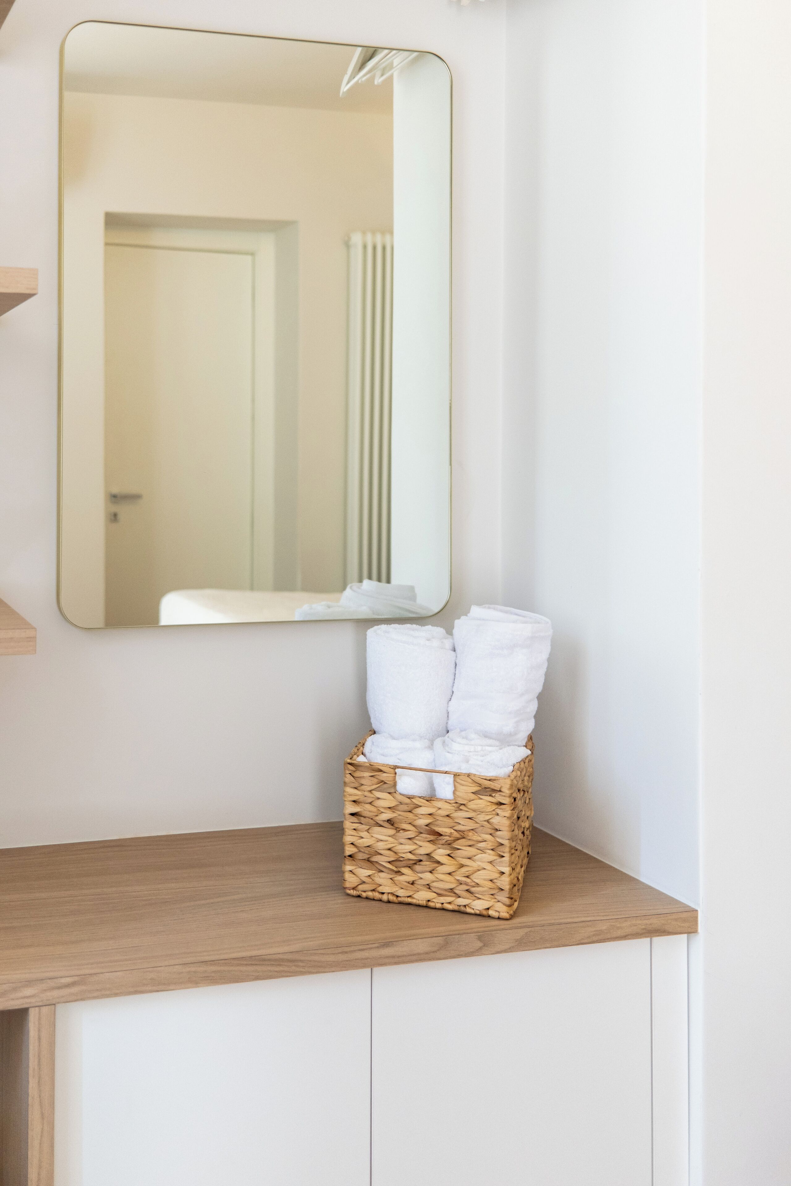 Een badkamer met een houten wastafelmeubel, een spiegel en een rieten mand met opgevouwen handdoeken.