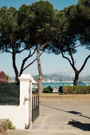 A coastal road with trees, a parking sign, and a distant view of the sea and mountains. - CADAMARE charming rooms in Portovenere (La Spezia)